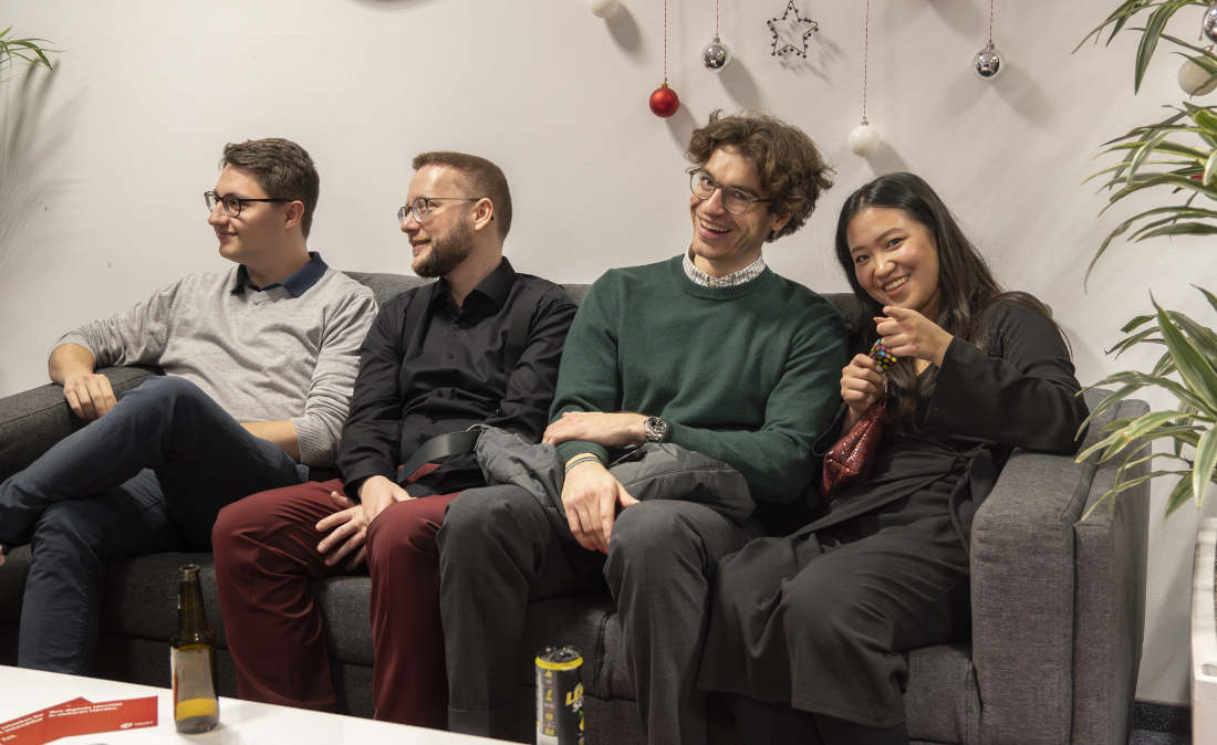 A-Trust employees sitting on a couch in front of a Christmas-decorated background